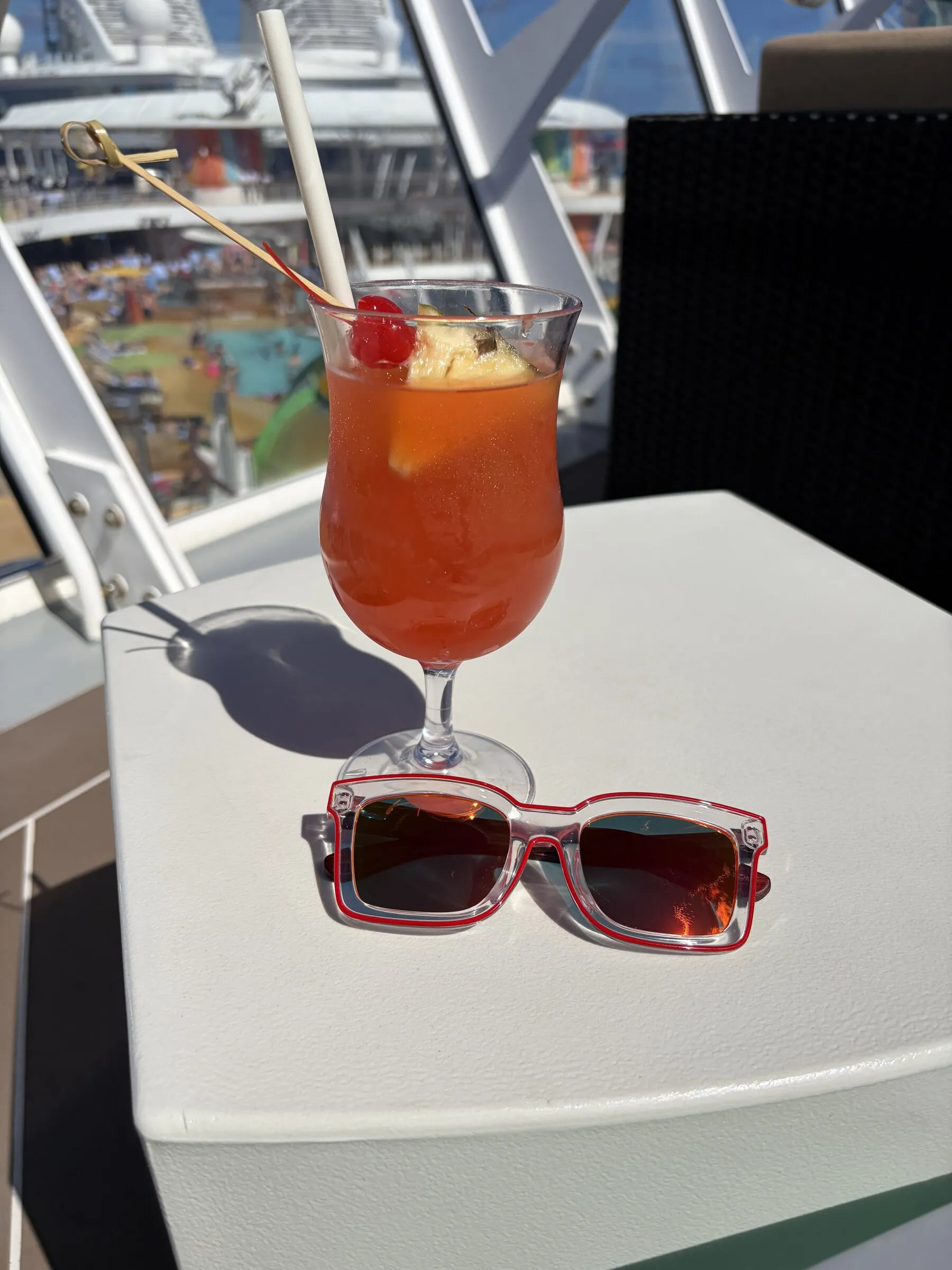 A tropical cocktail and sunglasses on a sunny cruise ship deck table